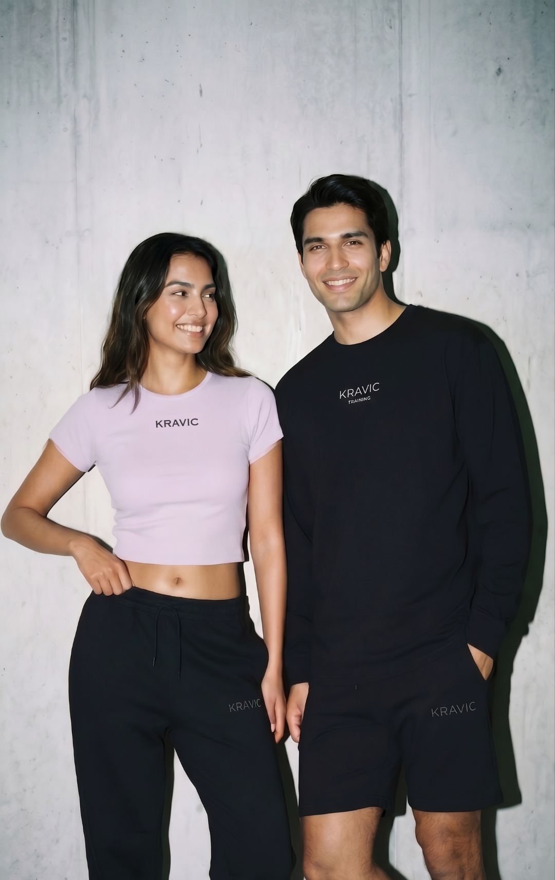 Two people wearing matching black and pink outfits with 'KRAVITZ' branding against a gray background.